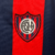 Camisa titular do San Lorenzo 2024-2025 azul marinho com duas faixas verticais vermelhas. Gola redonda e punhos vermelhos, ombros e mangas azul marinho. Escudo San Lorenzo com círculo central maior no peito esquerdo, logo Nike branco no direito.