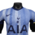 A nova camisa reserva dos Spurs 24/25 é azul clara com linhas verticais em vários tons de azul, inspirada no modelo de 92/94. A gola é V em azul marinho, cor das laterais. O escudo e logos são centralizados.