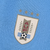 Camisa titular do Uruguai: azul celeste com design retrô. Gola V branca, abertura com botão. Tecnologia ULTRAWEAVE. Logo PUMA dourado nas mangas. Escudo AUF. 