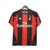 Camisa titular AC Milan 10/11 Adidas: vermelho e preto, com detalhes em dourado pela camisa. Dentro da gola, bandeira da Itália e escrito AC MILAN. Na nuca, bandeira italiana. Logo Adidas e escudo Milan bordados.