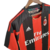 Camisa titular AC Milan 10/11 Adidas: vermelho e preto, com detalhes em dourado pela camisa. Dentro da gola, bandeira da Itália e escrito AC MILAN. Na nuca, bandeira italiana. Logo Adidas e escudo Milan bordados.