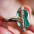 Anel elegante com uma grande pedra verde e detalhes em diamantes e pedras amarelas.