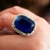 Anel com grande pedra azul surrounded by small diamantes e detalhes em ouro