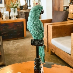 Pássaro decorativo feito de resina verde, posicionado sobre um elegante pedestal de madeira, exemplificando artesanato sofisticado e sustentável da Marcenaria Tiradentes.