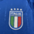 Camisa azul da seleção italiana de futebol, modelo 24/25, da Adidas, com detalhes em verde e vermelho nas mangas e escudo da Itália na parte frontal.