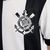 Kit infantil com camisa listrada em preto e branco e shorts pretos, ambos com o logo do Corinthians e da Nike.