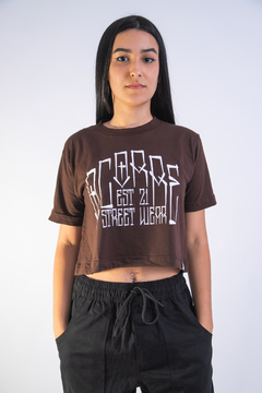 Camiseta cropped marrom com estampa em branco, usada por uma jovem.