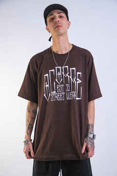 Modelo usando camiseta oversized marrom com estampa em branco, destacando a marca de streetwear.