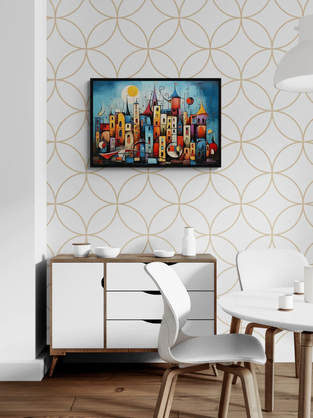 Um quadro decorativo numa sala de jantar com paredes decoradas por um papel de parede geométrico. A obra de arte apresenta uma cena colorida e estilizada de um aglomerado de casas multicoloridas com formas e tamanhos variados, sob um céu azul com a lua.