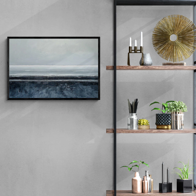 Um quadro decorativo numa parede de uma sala moderna, com prateleiras de madeira contendo objetos decorativos. A pintura mostra uma paisagem abstrata e minimalista de um mar tranquilo sob um céu nublado, com uma faixa escura no horizonte, em tons de cinza e azul.