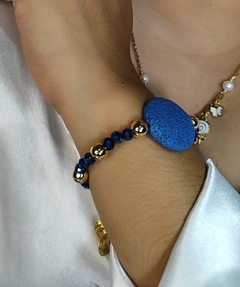 Pulsera con piedra volcánica acompañada de cristales azul metálico y separadores de chapa de oro, con un tamaño de 22cm aproximadamente.