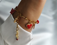 Pulsera con cristales rojos acompañado de separadores con chapa de oro, dijes de niña y niño en chapa de oro y dijes de latón. Cadena de acero inoxidable, la pulsera es de 22cm aproximadamente.