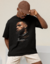 Camiseta oversized preta com estampa de LeBron James, apresentando seu rosto em perfil e detalhes de design com correntes e texto relacionado ao basquete.