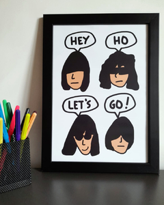 quadro com desenho do rosto dos integrantes da banda Ramones dizendo "hey ho let's go!", em tamanho A4, com moldura preta.
