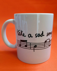 caneca branca com desenho de uma partitura e notas musicais com carinhas, e a frase "take a sad song and make it better"