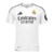 Camisa Real Madrid 2024/25: Vista frontal. Design branco com padrão houndstooth personalizado com iniciais RM. Detalhes pretos nas listras das mangas e gola V, representando a elegância e tradição do clube.