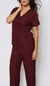 Modelo vestida com scrub  feminino bordô Vinho que esta à venda, ela esta de frente. O scrub é composto por uma blusa de manga curta com decote em V e dois bolsos frontais, e uma calça combinando.