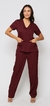 Modelo vestida de scrub feminino bordô vinho que esta à venda, ela esta de frente. O scrub é composto por uma blusa de manga curta com decote em V e dois bolsos frontais, e uma calça combinando. 