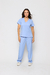 Modelo vestida de scrub feminino azul claro celeste, que esta à venda,, ideal para dentistas e profissionais da saúde. A blusa tem um decote em V, mangas curtas e dois bolsos frontais. A calça é solta e leve e possui um bolso.