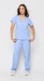 Esta imagem mostra uma modelo vestida de scrub feminino azul claro celeste, que esta à venda. O uniforme é composto por uma blusa de manga curta com decote em V e dois bolsos frontais, e uma calça combinando. Scrub é para hospital, clínica e home care.