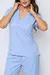 Modelo vestida de scrub feminino azul claro celeste , que esta à venda, composto por uma blusa de manga curta e uma calça na cor azul claro celeste. A blusa possui um decote em V, dois bolsos frontais e mangas curtas a calça é combinada e tem cordão.