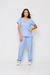 Modelo vestida de scrub feminino azul claro celeste, que esta à venda. O uniforme hospitalar scrub inclui uma blusa de mangas curtas com decote em V e dois bolsos frontais, combinada com calças soltas. A mulher está de pé, com uma mão no bolso