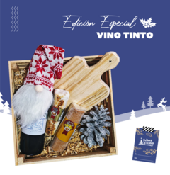 Vino tinto de 750 ml acompañado de un gorro navideño, un tabla de madera, dulces y decoraciones de invierno.