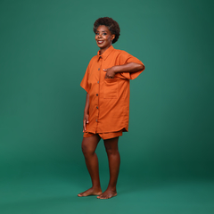 Imagem de modelo com manequim 38, altura de 1,55 e peso de 52 kg, usando o tamanho P de uma camisa oversized em linho na cor terracota. A peça apresenta bolso lateral, botões de casca de coco