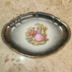 Prato decorativo antigo em porcelana com bordas douradas, destacando uma elegante cena romântica central.