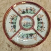 Prato decorativo oriental em porcelana com detalhes em dourado e divisórias, apresentando cenas tradicionais.