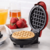 Panela elétrica waffle SmartElectric® com waffle cru e morangos frescos ao fundo.