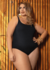 Modelo plus size usando um maiô preto, posando em frente a um fundo de madeira.