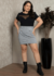 Modelo plus size usando uma blusa preta com decote redondo e recorte em tule, combinada com uma saia de estampas em preto e branco.