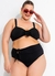 Modelo plus size usando um biquíni preto com detalhe em laço, óculos de sol vermelhos e colar de pérolas, sorrindo e fazendo um gesto de saudação.