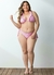 Mulher plus size sorridente usando um biquíni rosa com estampa de xadrez, posando em um fundo claro.