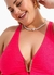 Modelo plus size sorrindo com um top rosa e colar de pérolas.