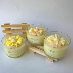 Conjunto de velas aromáticas em copos de vidro, com detalhes decorativos em amarelo, apresentando os rótulos 'Cereja e Avelã' e 'Cascas e Folhas'.