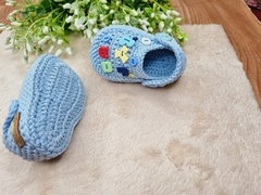 Mini crocs de crochê azul para bebê com letras coloridas decorativas.