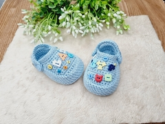 Mini crocs de crochê azul para bebê com letras coloridas decorativas.