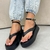 Sandálias flatform na cor preta, com detalhes de tiras e salto alto, usadas com calça jeans clara.