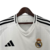 Imagem da camisa titular Real Madrid 24/25, com design branco tradicional, gola em V e detalhes em dourado e azul marinho.