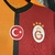 Imagem da camisa titular do Galatasaray 2024/2025 Puma com design meio a meio em laranja e amarelo, detalhes em preto e logo da Puma em vermelho.