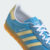 Tênis ADIDAS GAZELLE INDOOR na cor azul com detalhes em amarelo e sola translúcida.