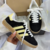 Tênis ADIDAS GAZELLE INDOOR na cor preto com detalhes em amarelo, modelo com três listras laterais e sola translúcida.