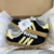 Tênis ADIDAS GAZELLE INDOOR na cor preto com detalhes em amarelo, modelo com três listras laterais e sola translúcida.