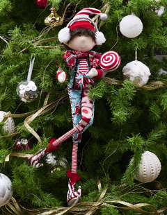 Duende de Navidad con overol, orejeras y paleta de caramelo, decorando un árbol de Navidad.