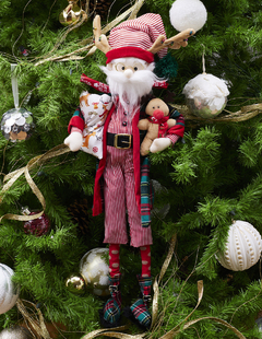 Muñeco de Santa Claus con pijama de rayas rojas y blancas, sosteniendo un reno de peluche y una almohada decorativa.