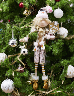 Duende de Navidad rosa con balón de fútbol y señal de "North Pole" colgando de un árbol decorado.