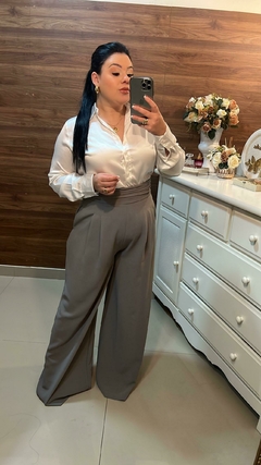 Mulher posando com camisa branca e calça cinza larga em um ambiente com decoração elegante. Pantalona, calça pantalona, calça cinza, pantalona cinza, calça cinza, cor cinza, cor do momento, cor  básica, cor neutra, cinza, cinza gelo, calça cintura alta