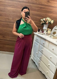 Uma mulher posando em um espelho, vestindo uma blusa verde e calças largas bordô, em um ambiente com decoração elegante. Pantalona, calça pantalona, pantalona cor roxa, cor rosa, calça roxa, calça rosa, 